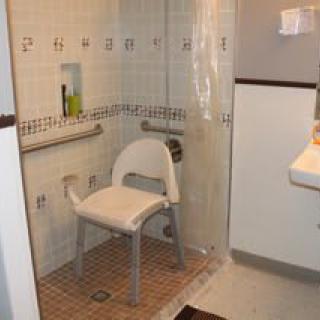 An accessible bathroom with a shower chair and grab bars for safety.