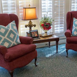 A cozy living room setup featuring two comfortable armchairs with decorative pillows, a lamp, and a small table adorned with flowers.