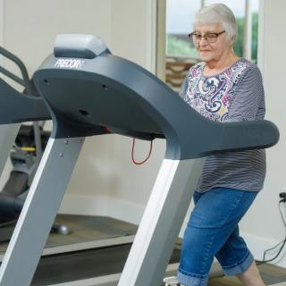 An elderly woman exercising on a treadmill in a gym setting.