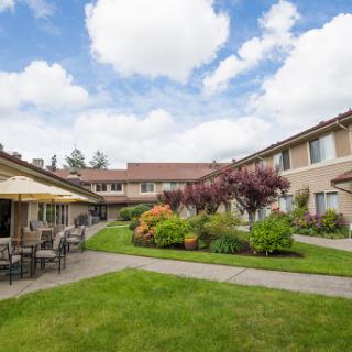 A tranquil courtyard with comfortable seating surrounded by vibrant plants and a picturesque sky.