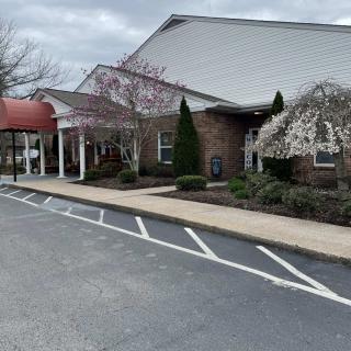 A building with a covered entrance and adjacent parking area on a cloudy day.