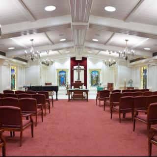 Interior view of a synagogue with rows of seating, stained glass windows, and a pulpit.