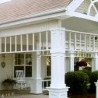 A white porch with columns and a sloped roof, featuring a rocking chair and plants.