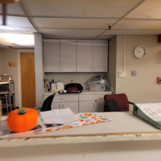 A cozy office space featuring a small pumpkin on the desk and a kitchenette in the background.