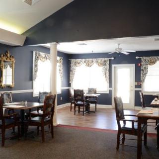 A cozy dining area with elegant decor, featuring multiple tables and chairs set against large windows with decorative curtains.