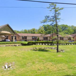 A roadside motel with a neatly maintained lawn and trees under a clear blue sky.