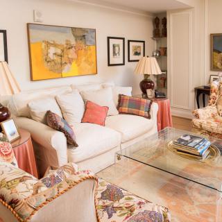 A cozy living room with a beige sofa, decorative pillows, and warm lighting. The space features colorful artwork and elegant furnishings.
