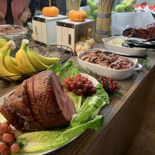 A buffet table showcasing a variety of foods including a sliced ham, bananas, grapes, and other dishes.