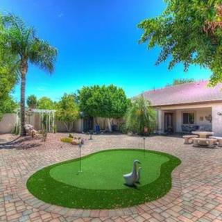 A beautifully landscaped backyard featuring a small putting green, surrounded by palm trees and a spacious patio.
