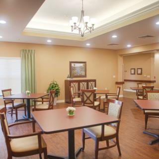 A cozy dining room with neatly arranged tables and chairs, featuring warm lighting and wooden flooring.