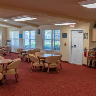 A spacious dining area with multiple tables and chairs, featuring large windows and a red carpet.