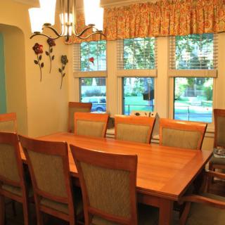 A cozy dining room with a wooden table and chairs, featuring large windows and a decorative light fixture.