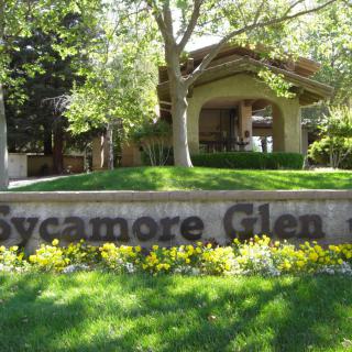 A welcoming entrance to Sycamore Glen surrounded by lush greenery and trees.