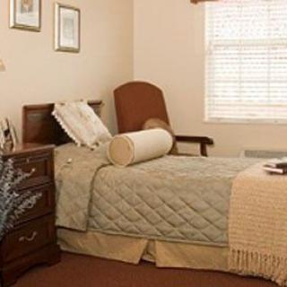 A cozy bedroom with a bed, armchair, and nightstand beside a window.