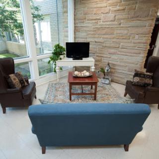 A cozy living room setup featuring a blue sofa, brown chairs, a small table, and a television against a backdrop of large windows.