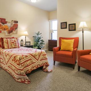 A cozy bedroom with a bed, two armchairs, and warm decor elements.