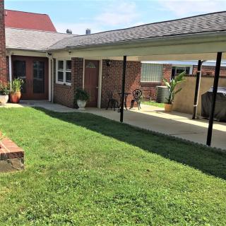 A backyard with a well-maintained lawn, a brick house, and a covered patio area.