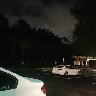 A quiet parking lot illuminated by faint lighting under a cloudy night sky.