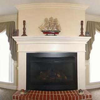 A traditional fireplace with a white mantel, adorned with a model ship and candles, set above a brick hearth.