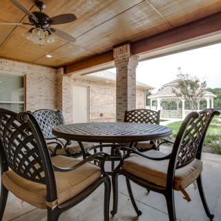 A cozy covered patio with a round table and four chairs, featuring a ceiling fan and view of the backyard.