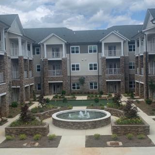 A modern apartment complex with a central courtyard featuring a fountain and landscaped greenery.