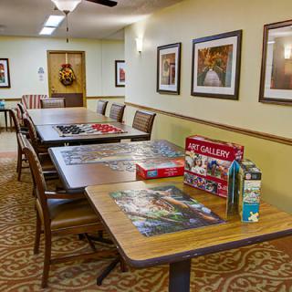 A cozy community room with tables, chairs, and puzzles set up for leisure activities.