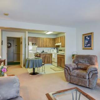 A cozy living room with an open kitchen layout, featuring comfortable armchairs and warm decor.