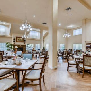 A spacious and well-lit dining room with multiple tables and chairs arranged neatly, illuminated by elegant chandeliers.