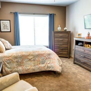 A cozy bedroom with a bed, dresser, and window with blue curtains.