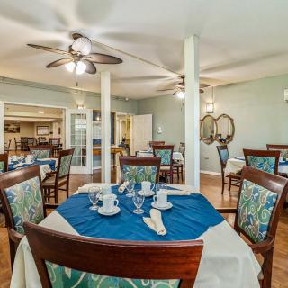 A well-decorated dining area with tables and chairs, featuring elegant place settings and ceiling fans.