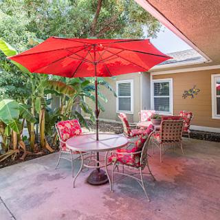 A cozy outdoor patio setup featuring a vibrant red umbrella and comfortable seating surrounded by lush greenery.