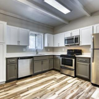 A modern kitchen showcasing sleek white cabinets and stainless steel appliances, complemented by stylish wood flooring.