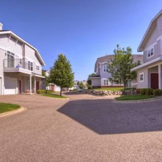 A peaceful residential neighborhood featuring modern homes and well-maintained landscaping under a clear blue sky.