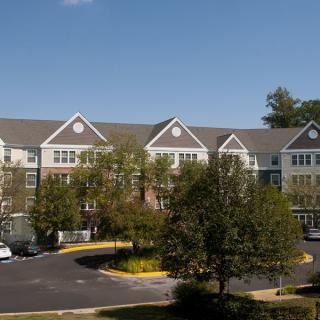 A residential apartment building with a parking lot and trees under a clear blue sky.