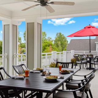 A cozy outdoor patio with a dining area, featuring a table set for a meal and a red umbrella providing shade.
