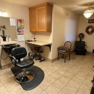 A cozy barber shop interior with a styling chair, mirror, and various furnishings.