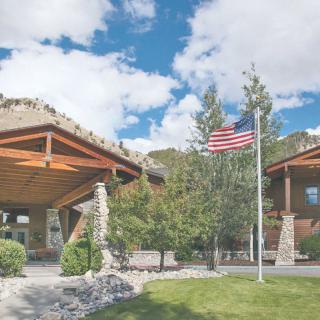 A wooden building with a U.S. flag in a landscaped area surrounded by trees and clouds.