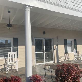 A sunny porch with rocking chairs and a building entrance, surrounded by plants.