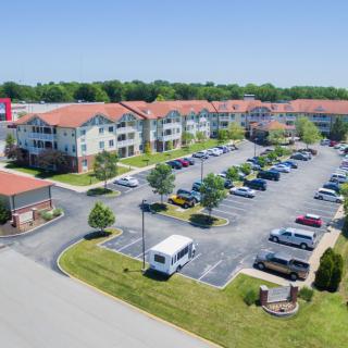 Aerial view of an apartment complex with a parking lot surrounded by greenery.