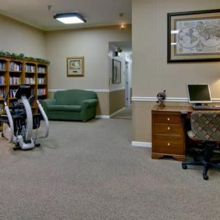 An office space featuring a desk with a laptop, a sofa, bookshelves, and exercise equipment.