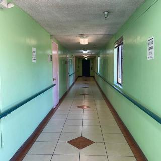 A long, well-lit hospital corridor with green walls and tiled flooring.