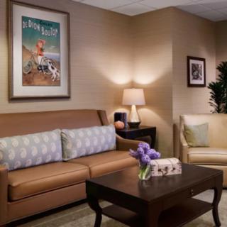 A cozy living room with a sofa, armchair, and coffee table, decorated with artwork and a lamp.
