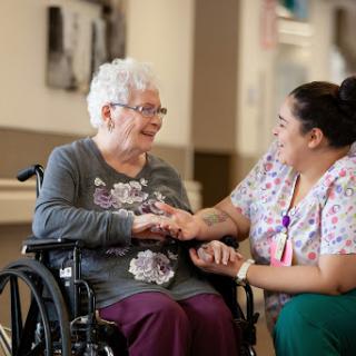 A caregiver engages warmly with an elderly woman in a wheelchair, showcasing the importance of companionship and support in healthcare.