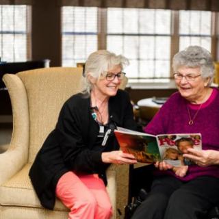 Two women enjoying a magazine together in a cozy indoor setting.