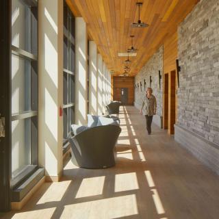 A modern hallway with large windows, stone walls, and wooden ceiling, featuring comfortable seating.