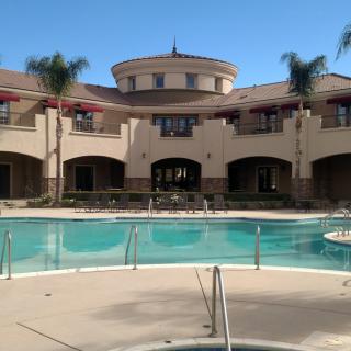 A luxurious building with a large outdoor swimming pool surrounded by palm trees under a clear blue sky.