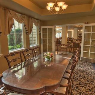 A spacious dining room with a large wooden table and elegant chandeliers, featuring French doors and tasteful curtains.