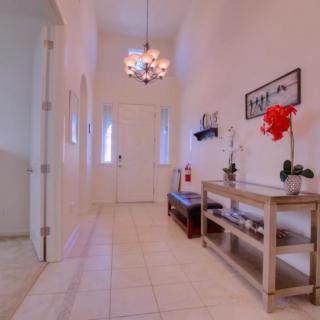 A bright hallway with white walls, a chandelier, and a wooden console table adorned with plants.