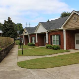 A row of suburban houses with neatly trimmed lawns and a paved sidewalk on a clear day.