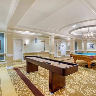 A luxurious game room featuring a shuffleboard table and a pool table under an elegant chandelier.